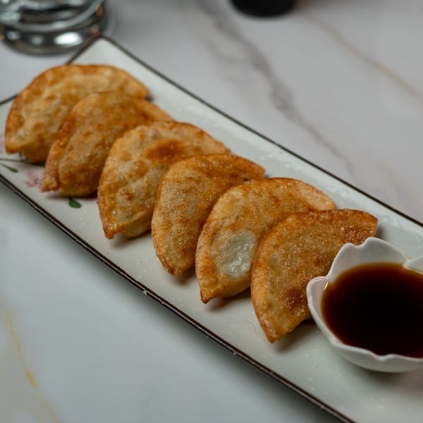 Golden-brown fried dumplings arranged on a rectangular plate with a small dish of soy sauce.