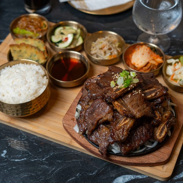 Korean BBQ short ribs, rice, and various banchan in small gold bowls on a wooden board.