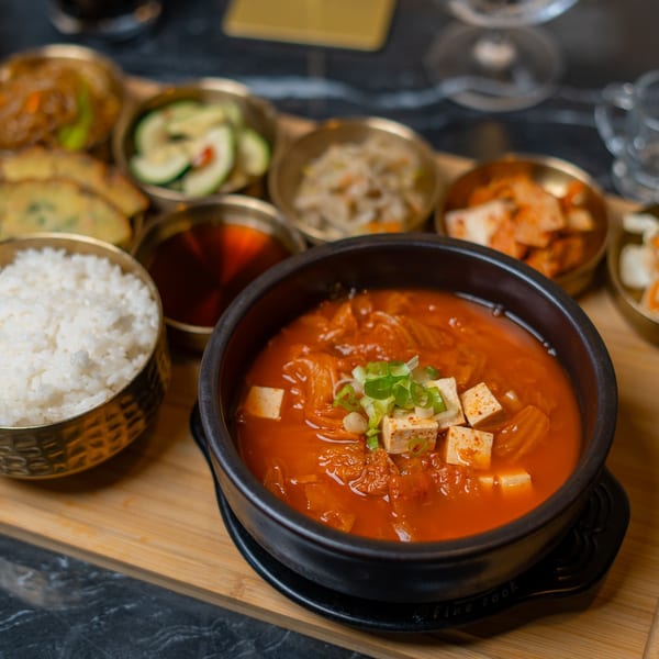 A Korean meal set with kimchi jjigae, rice, and various banchan on a wooden tray.